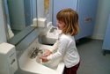 TOD361FM 003 001-Smiling White Pre-k girl standing alone in restroom at school washes paint off her hands after completing her art project